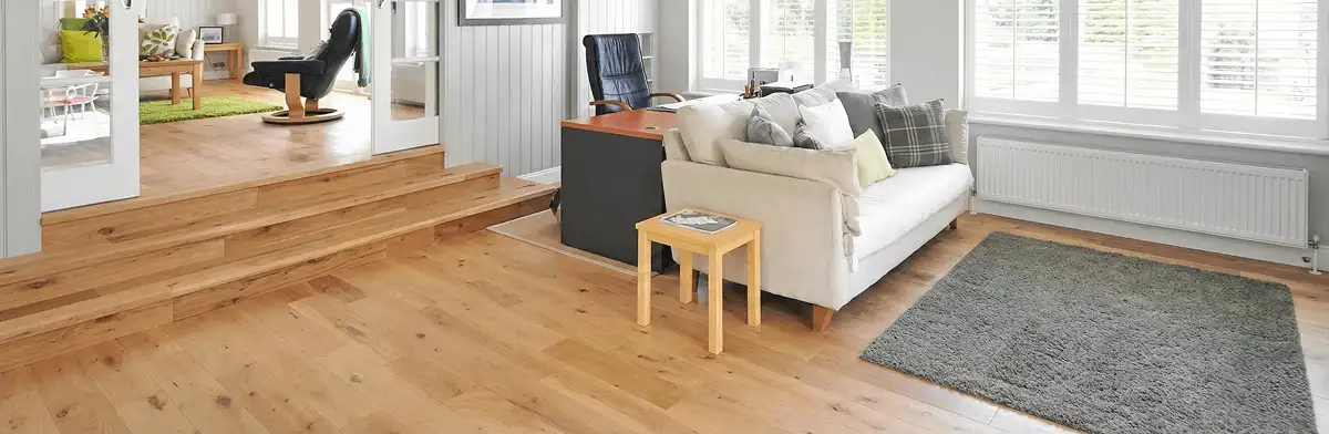 A modern living room with professionally installed laminate flooring, a beige sofa, a small side table, a gray rug, and large windows with white shutters in Manchester, NH